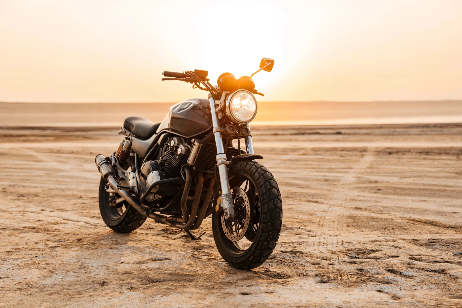 A classic motorcycle parked on sand in warm evening light.