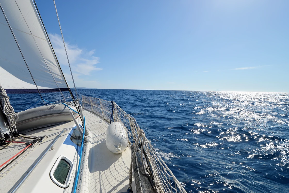 White sailing yacht deck and open sea in sunlight.