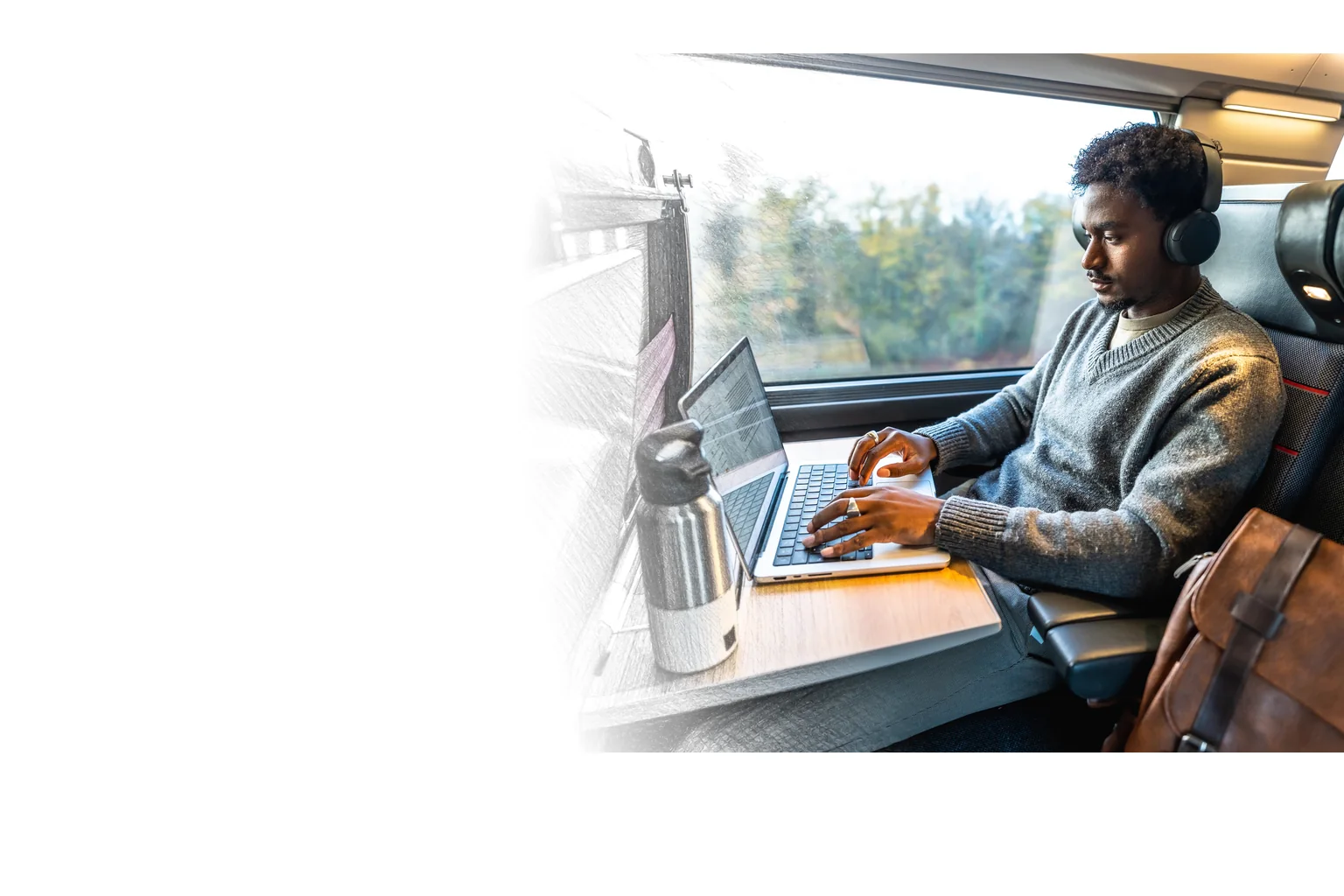 A traveler works on a laptop at a train table by the window, with trees passing outside.